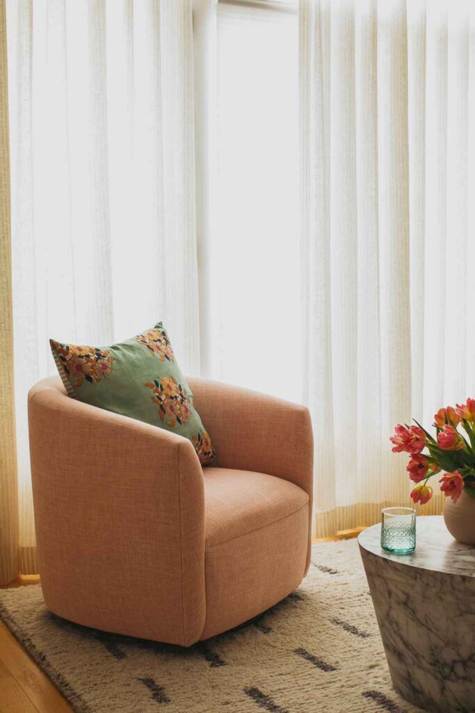 kp-home-60091-logan-square-home-tour-coral-colored-upholstered-chair-in-living-room-by-window-sheer-drapes-patterned-rug-contemporary